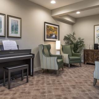 A cozy living room featuring a piano, armchairs, and framed artwork on the walls.