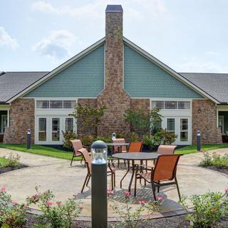 A cozy outdoor patio with seating set against a building with a stone facade and landscaped garden.