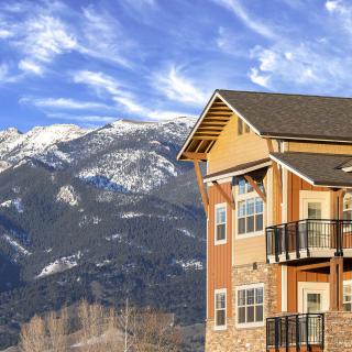 A modern house with balconies set against a backdrop of snow-capped mountains and a clear blue sky.
