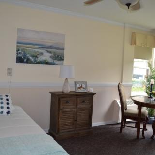 A cozy bedroom with a bed, wooden dresser, and a small table with chairs by the window.