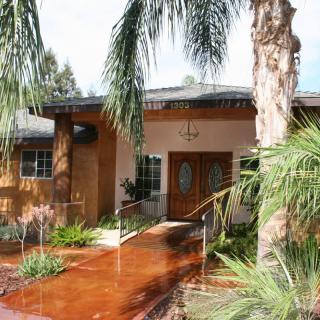 A welcoming house entrance surrounded by palm trees and lush landscaping.