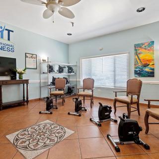 A well-lit fitness room with chairs and exercise equipment, featuring a TV and colorful wall art.