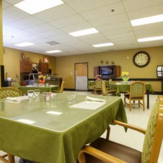 An empty dining area with green tablecloths, a clock on the wall, and a television.
