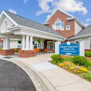 A welcoming entrance to a modern building with a sign, surrounded by well-maintained landscaping under a blue sky.