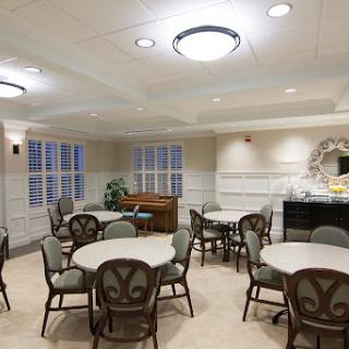 A cozy dining area featuring round tables and comfortable chairs, illuminated by modern light fixtures.