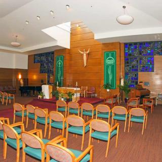A modern chapel interior featuring rows of chairs, an altar, and stained glass windows.