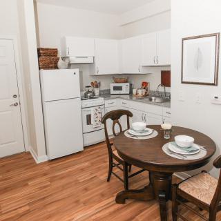 A cozy kitchen and dining area featuring a small round table set for two, with white cabinets and essential appliances.