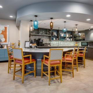 A modern kitchen with a stylish bar area featuring bright chairs and pendant lighting.