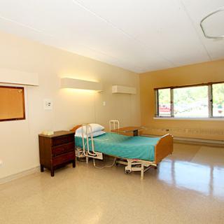 A clean and simple hospital patient room featuring a single bed and natural light from the window.