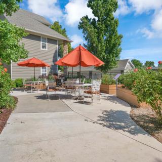 A sunny outdoor patio area with tables, chairs, and orange umbrellas next to a house.