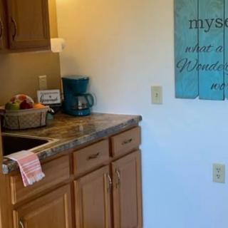 A cozy kitchen corner with a coffee maker, fruit basket, and decorative sign.