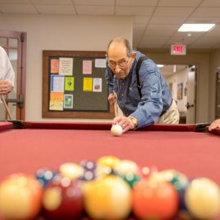 An elderly man focuses intently as he prepares to take a shot in a game of pool.