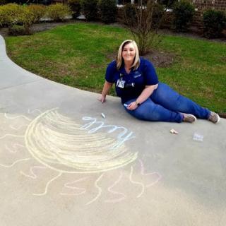 A woman enjoys creating colorful sidewalk chalk art while lying on the pavement.