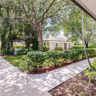 A residential house with a landscaped yard, featuring trees and a concrete pathway under sunlight.