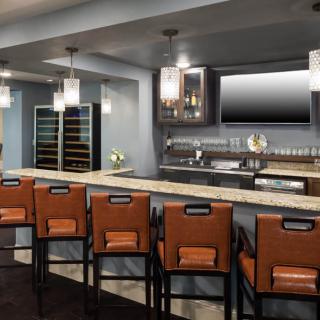 A modern bar with sleek design elements, featuring a marble counter, comfortable stools, pendant lighting, and a wine storage area.