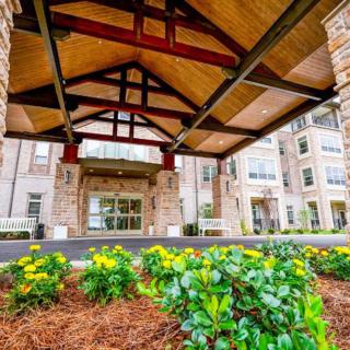 A beautifully landscaped building entrance with a wooden canopy and vibrant flowers.