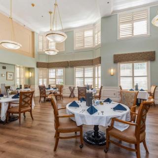 A spacious and elegant dining room with well-arranged tables and chairs, featuring large windows that allow natural light to brighten the space.