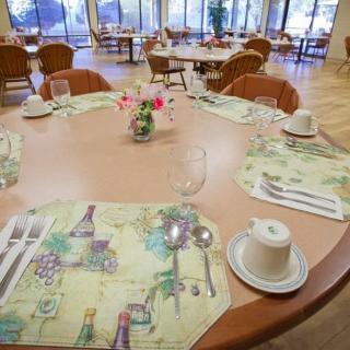 A neatly set dining table in a restaurant, featuring colorful place mats, cups, and a floral centerpiece.