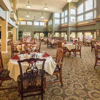An elegant dining area with set tables and chairs, featuring large windows allowing natural light to enter.