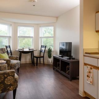 A cozy living room with a TV, chairs, and a small dining area by the windows.