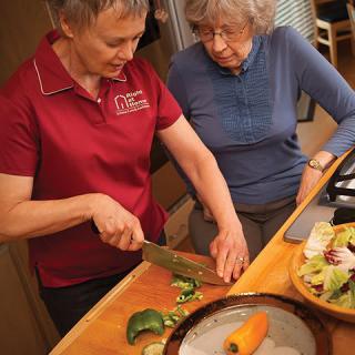 Two people preparing a meal together in the kitchen, chopping vegetables for a salad.