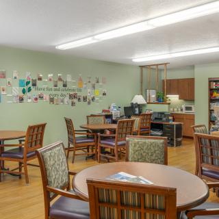 A comfortable dining area with round tables and chairs, featuring a decorative wall and adjacent kitchen facilities.