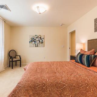 A cozy bedroom with warm-toned bedding, featuring a decorative chair and wall art.