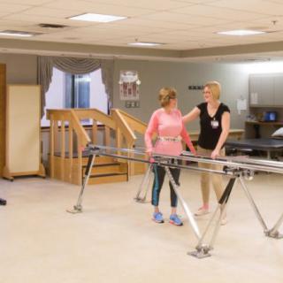 A physical therapy session with a therapist assisting a patient using parallel bars.
