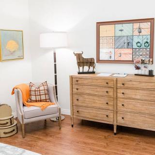 A cozy, modern bedroom with a wooden dresser and chair, accented by warm lighting and wall art.
