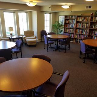 A quiet library reading room with tables, chairs, and bookshelves.