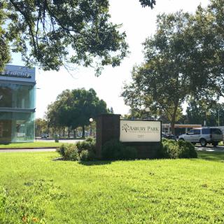 A sign in front of a building surrounded by greenery.