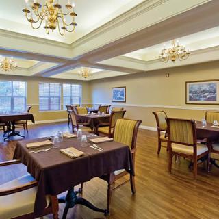 An elegant dining room with tables set for a meal, featuring chandeliers and a wooden floor.