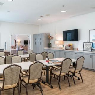 A modern meeting room with tables and chairs arranged for a conference, featuring a television and stylish decor.