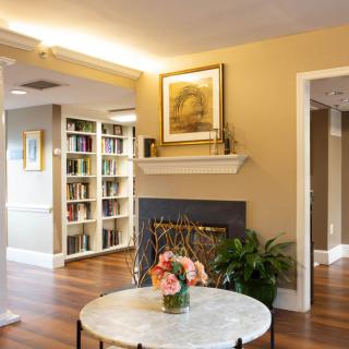 A cozy living room with a fireplace, bookshelves, and decorative flowers on a table.