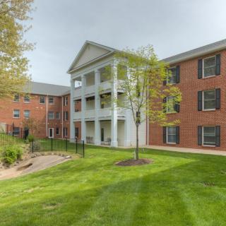 A view of a residential apartment building with brick exterior, surrounded by green grass and trees.