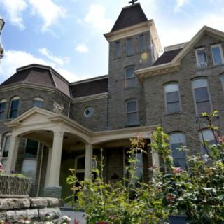 A historic stone building with Victorian architectural elements and a garden in the foreground.