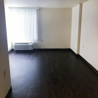 An empty room with hardwood floors and a large window offering natural light.