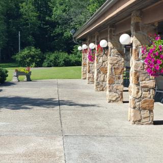 A sunny outdoor patio with stone pillars, hanging flower baskets, and a nearby garden bench.