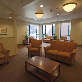 A comfortable waiting area with sofas and chairs arranged around a coffee table, illuminated by overhead lighting.
