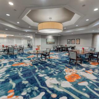 A modern dining area with tables and chairs, featuring a colorful carpet and elegant lighting.
