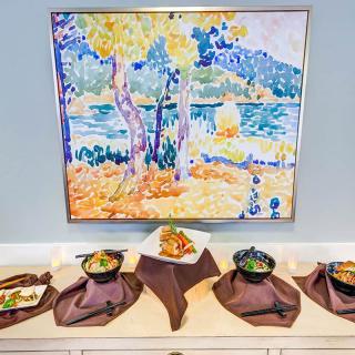 A buffet setup with various dishes placed under a vibrant landscape painting.