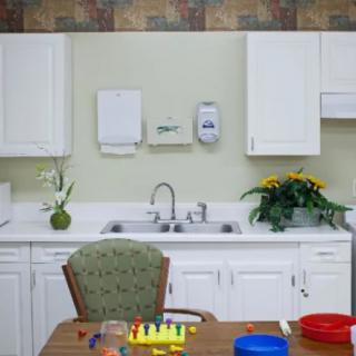 A small kitchen area with a sink, white cabinets, and a table with toys in the foreground.