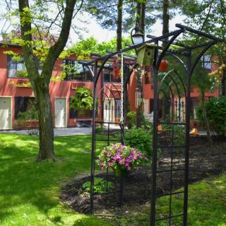 A tranquil garden with an archway, lush greenery, and a backdrop of a red building.