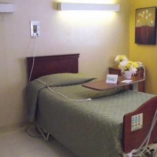 A hospital room featuring a single bed with attached medical equipment and a small table with flowers.