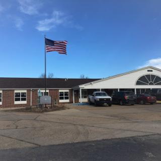 A view of a building with an American flag flying, surrounded by parked vehicles under a clear blue sky.
