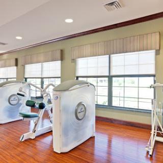 A well-lit gym area featuring strength training equipment and large windows for natural light.