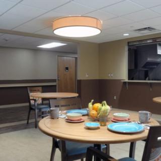 A dining room setup with tables and chairs, featuring a centerpiece of fruits and arranged plates.