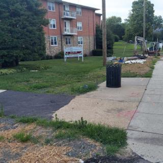 A view of an apartment complex with a sidewalk, grassy area, and a trash can.