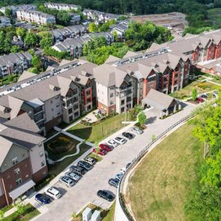 Aerial view of suburban apartment buildings with a parking lot and surrounding greenery.