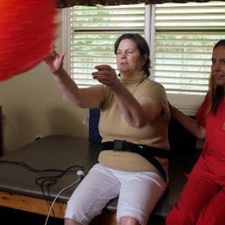 A caregiver assists an elderly woman in a therapy session, promoting physical activity and engagement.
